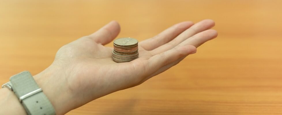 Open hand holding Thia coin on wooden table in background.