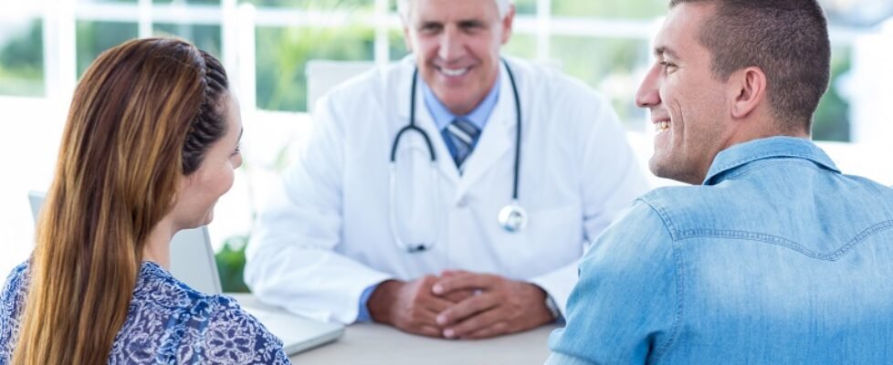 Smiling doctor looking at happy couple in medical office