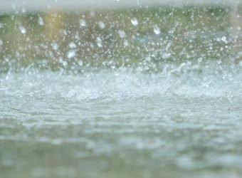 Rain drops falling in a big puddle on urban asphalt in the town.