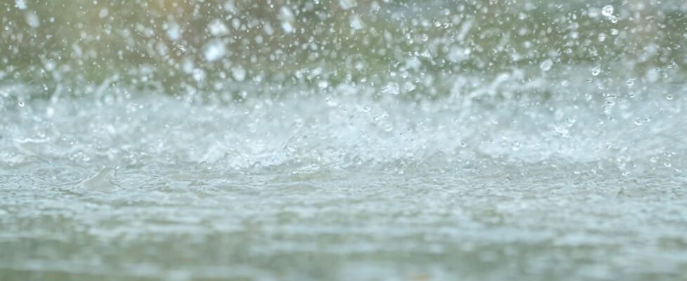 Rain drops falling in a big puddle on urban asphalt in the town.