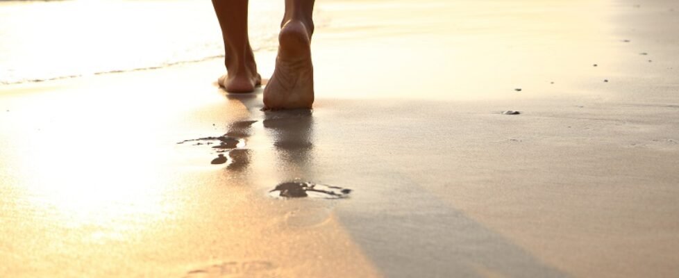 Girl walking on wet sandy beach leaving footprints