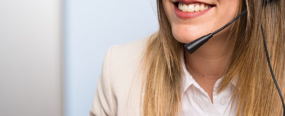 Young blonde telemarketer woman over isolated blue wall and smiling
