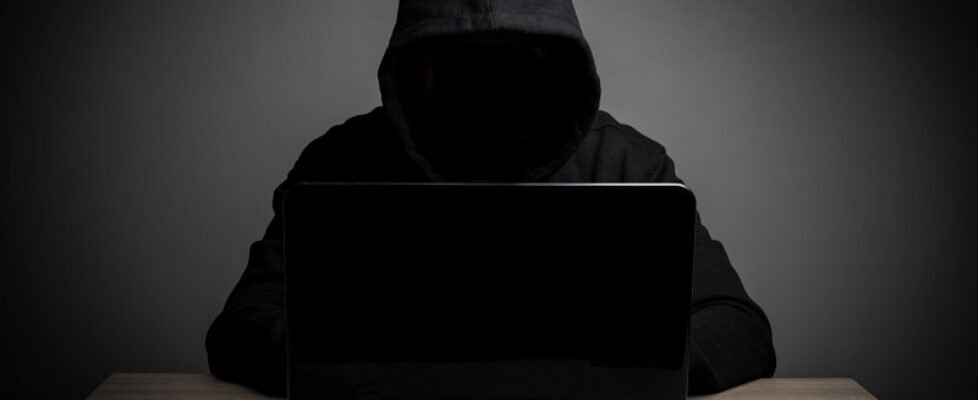 Hacker work front of his laptop computer with dark face.