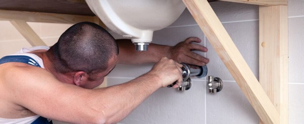 Closeup male plumber worker in blue denim uniform, overalls, fix