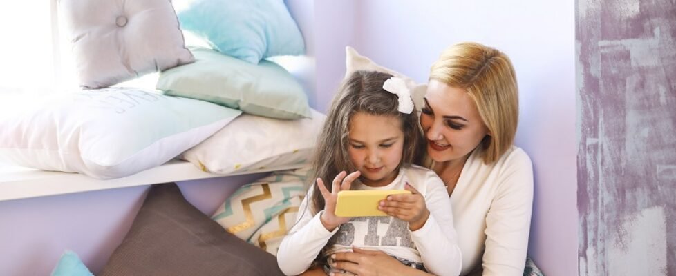 Happy mother and daughter are watching smth on the smartphone an