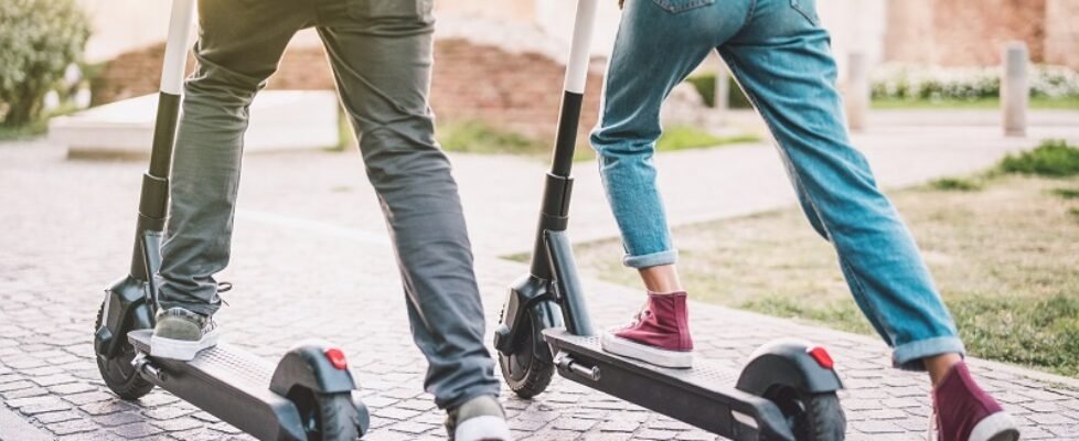 Close up of people couple using electric scooter in city park - Millenial students riding new modern ecological mean of transport - Green eco energy concept with zero emission - Warm sunshine filter