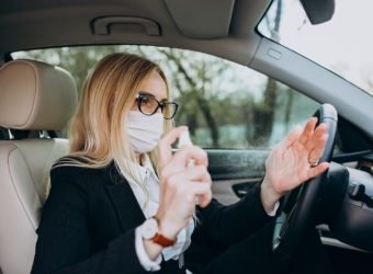 Business woman in protection mask sitting inside a car using antiseptic