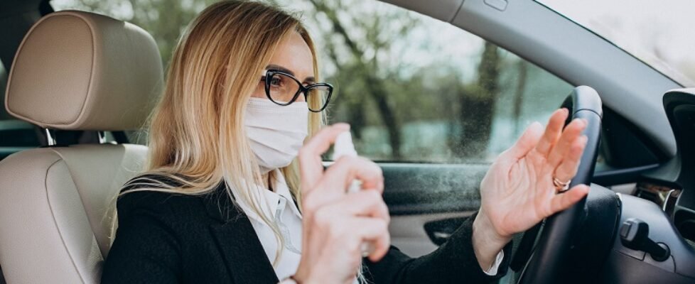 Business woman in protection mask sitting inside a car using antiseptic