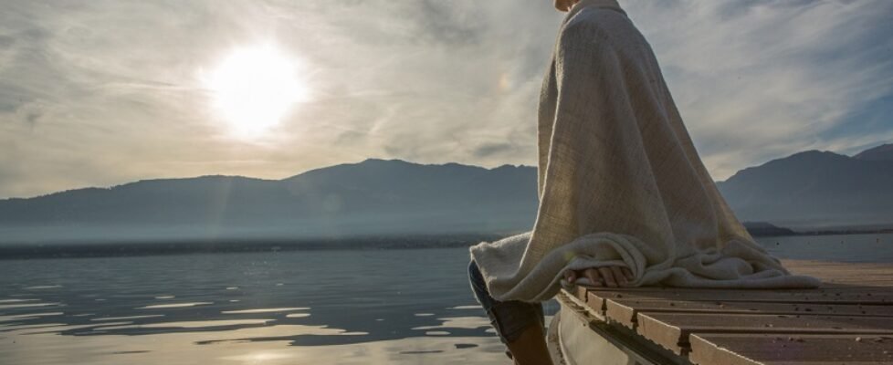 Young woman relaxes on lake pier with blanket, watches sunset