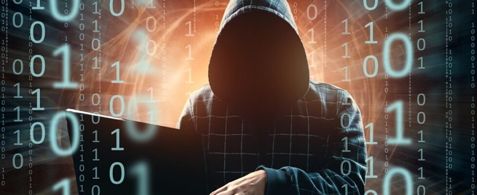 A man in a hood, a hacker, a hacker attack, a silhouette of a man, holds a laptop, threatens. mixed media. The concept of sudden attack, cryptography, data security.