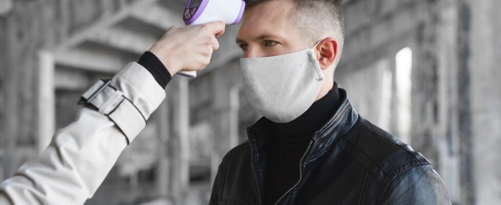 Operator check fever by digital thermometer visitor at information counter for scan and protect from coronavirus COVID-19