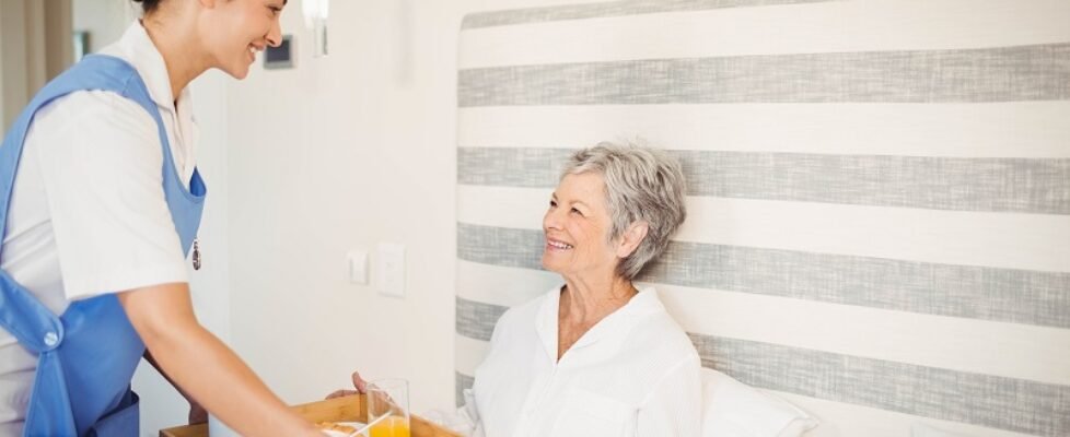 Nurse serving breakfast to senior woman in bedroom
