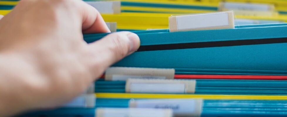 Closeup of a hand search and select a file folder from a group of file folders on shelves in an office