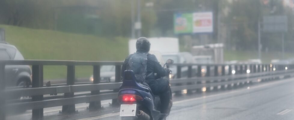 A man riding his scooter in the rain, a lifestyle of people living in urban area. road with metal safety rail