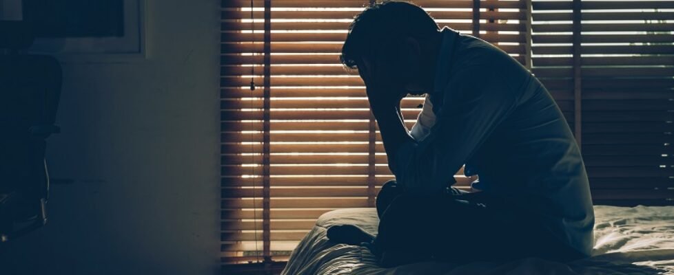 Sad businessman sitting head in hands on the bed in the dark bed
