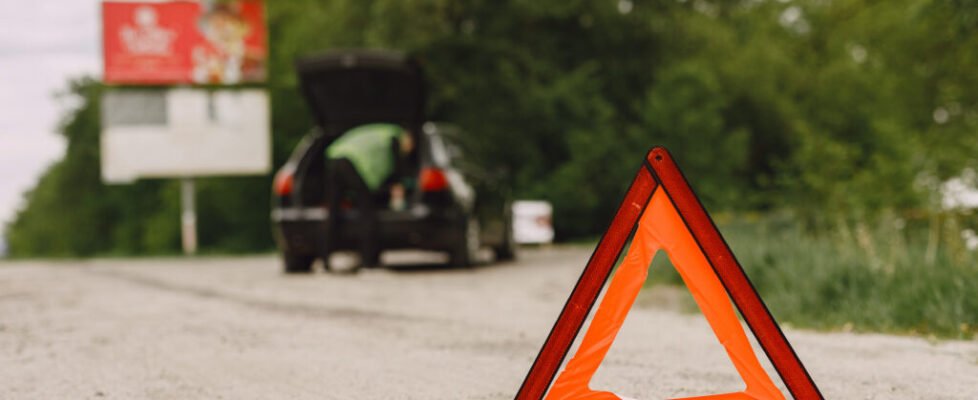 Driver putting warning triangle on asphalt road. Emergency stop concept.