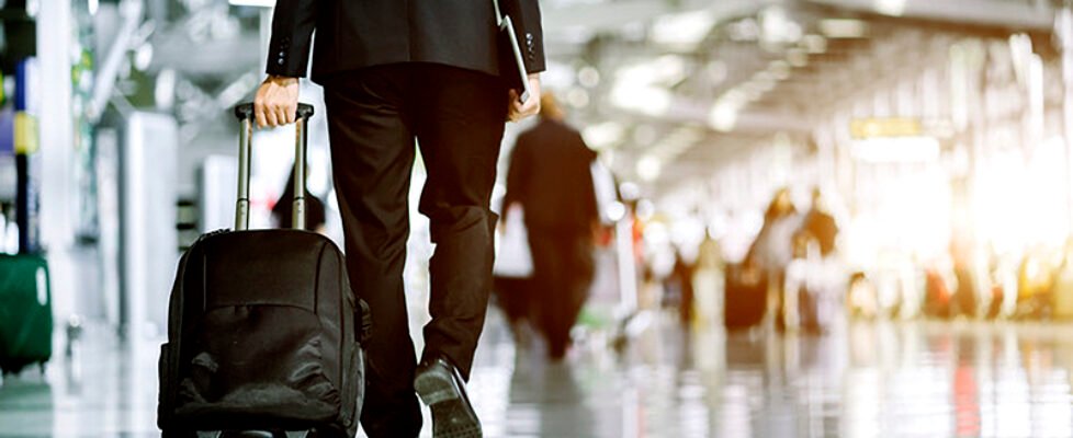 Businessman checking e-mail on mobile phone while walking with suitcase inside airport