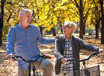 Happy elderly couple riding a bicycle in the park in the autumn