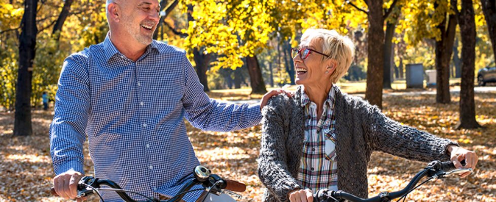 Happy elderly couple riding a bicycle in the park in the autumn