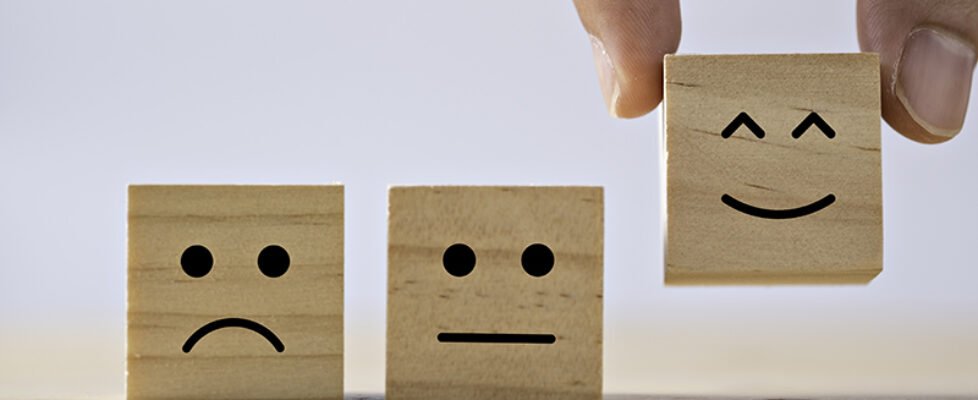 Hand putting smiley emotion to among normal and sad emotion whic