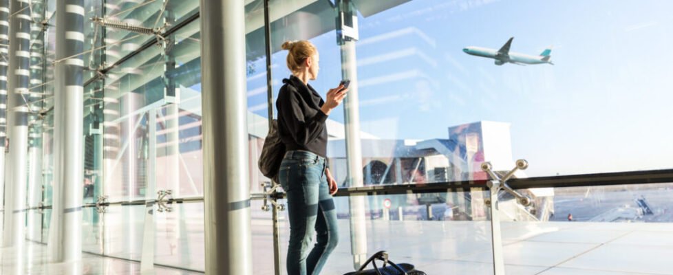 Young woman waiting at airport, looking through the gate window.