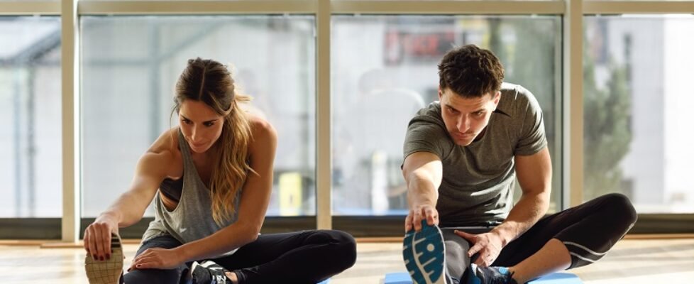 Two people streching their legs in gym.