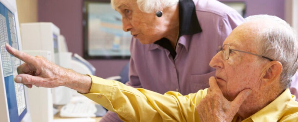 Senior woman helping senior man use computer