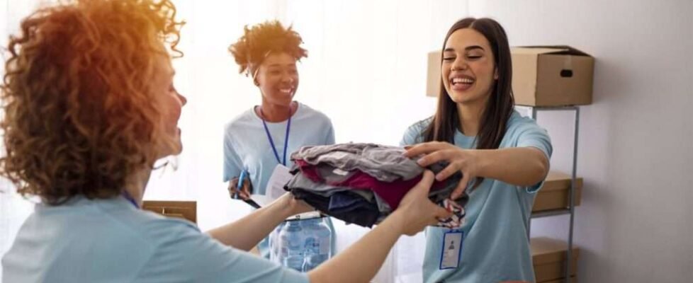 Volunteers Collecting Food Donations In Warehouse. Happy team of volunteers holding donations boxes in a large warehouse. Volunteers putting clothes in donation boxes, social worker making notes charity
