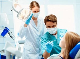 A dentist and a nurse treat a patient in a dental office. They put on medical masks