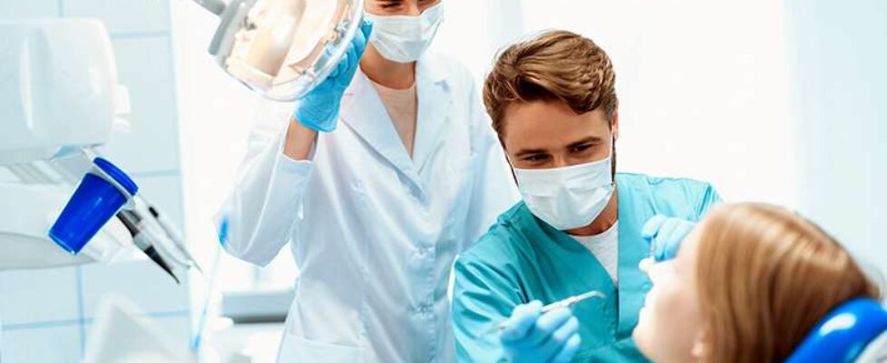 A dentist and a nurse treat a patient in a dental office. They put on medical masks