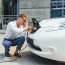 Hansome guy sitting near his new modern electric car and holding plug of the charger, while car is charging at the charging station