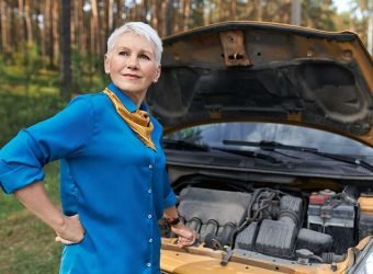 Portrait of mature female with blonde short hair having frustrated facial expression because car in broken. Stressed middle aged woman waiting for service after vehicle breakdown, opening hood