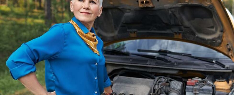 Portrait of mature female with blonde short hair having frustrated facial expression because car in broken. Stressed middle aged woman waiting for service after vehicle breakdown, opening hood