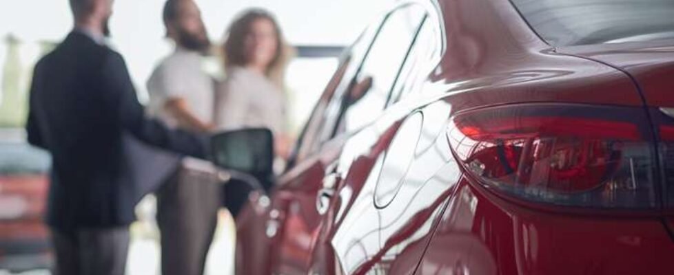 Red car close up, clients of car dealership behind.