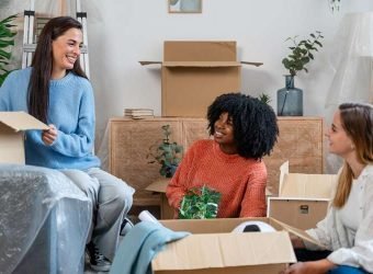 smiling multiethnic women unpacking cardboard boxes at new home
