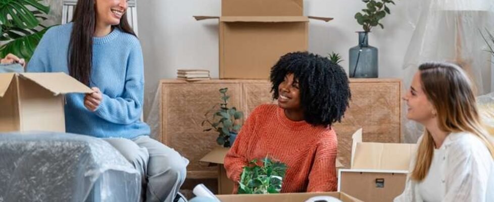 smiling multiethnic women unpacking cardboard boxes at new home