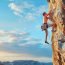 A man rock climbing on a cliff face against a blue sky with clouds.