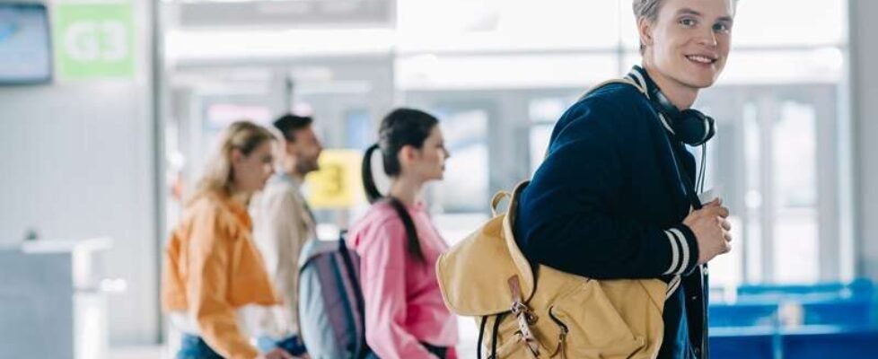 handsome young man with backpack smiling at camera while traveling with friends