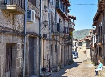 An old woman alone sitting on a bench enjoys a sunny day on an empty street. It reflects the depopulation of rural areas in Spain due to lack of employment.
