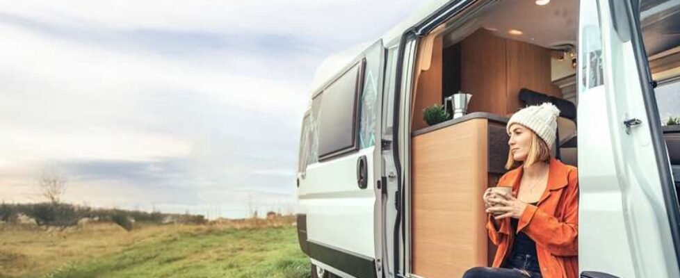 Woman drinking coffee sitting at the door of a campervan