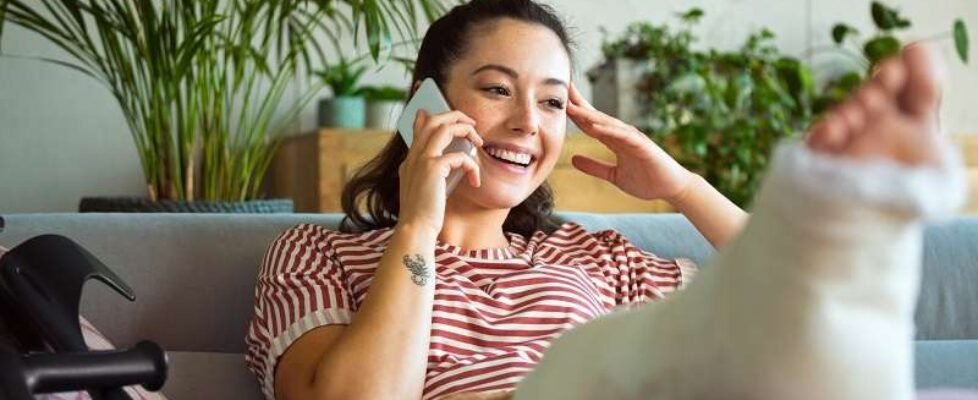 Cheerful young woman with broken leg on phone